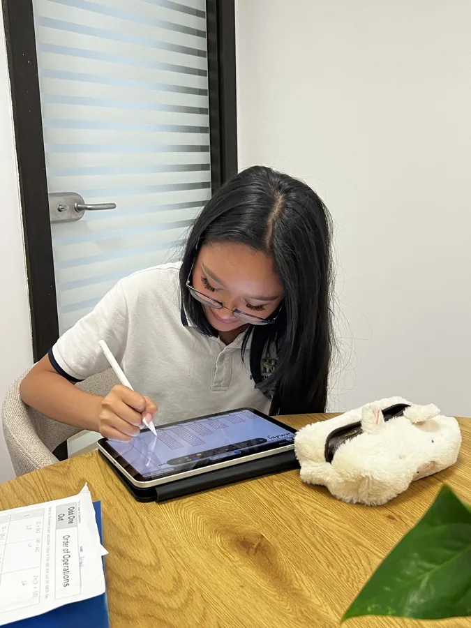 Kinan working on her tablet at a round oak table in the house