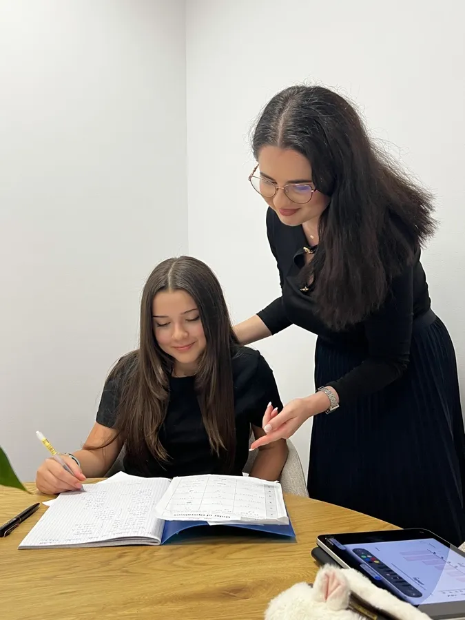 Yasemin smiling over her notebook as Ms Patricia, her mentor, looks on beside her
