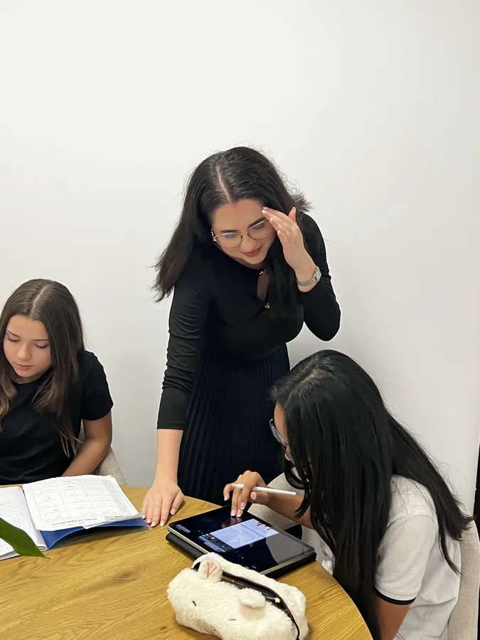 Yasemin and Kinan working at a round oak table, with Ms Patricia, their mentor, between them